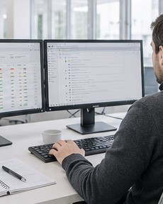 Technician at a two-monitor workstation reviewing a monitoring dashboard